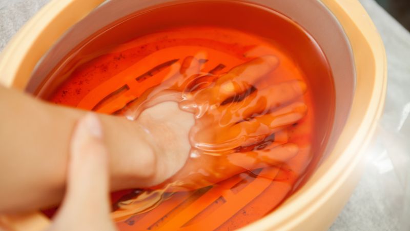 Parafínová vana s teplým parafínovým zábalem na ruce, ideální pro hydrataci a změkčení pokožky.